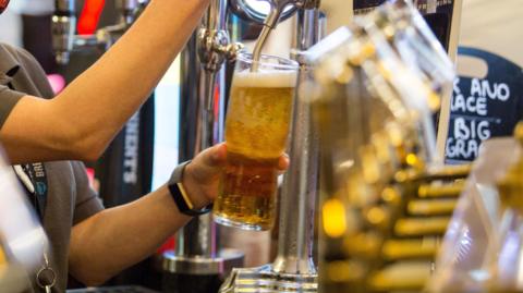 A view of a person pulling a pint of golden beer behind a bar with several silver pumps. 