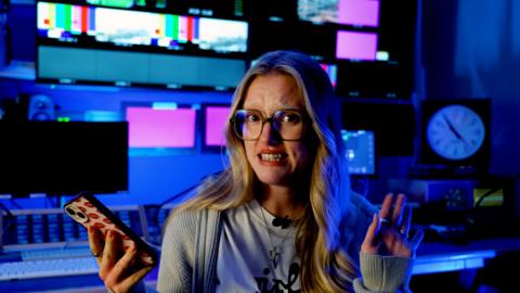 A woman with a p0hone in her hand looking at the camera