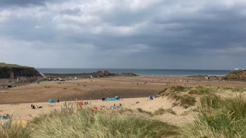 People enjoying a beach in Bude, with sand dunes in the foreground and the sea in the distance