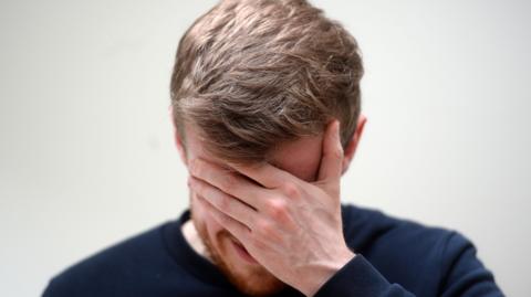 A man hides his face with his hand in a scene of distress.