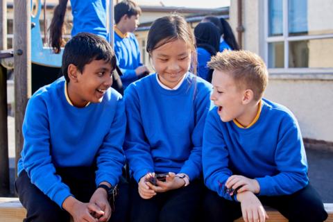 Three children sit in their playground with micro:bits