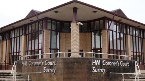 The outside of Surrey Corner's Court which has tall glass windows on each side and a triangular canopy protruding. A low wall in front of the building has the name of the court on it in large letters and there are steps leading up to the court