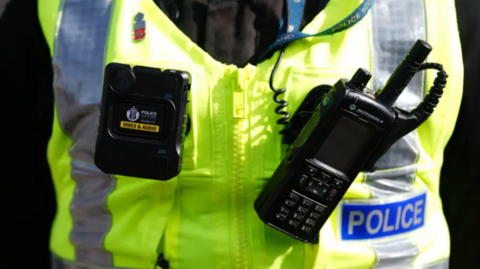 A medium close up of a police officer in a high vis vest with a radio attached.