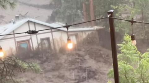 A house is swept along a brown river of raging flood water.