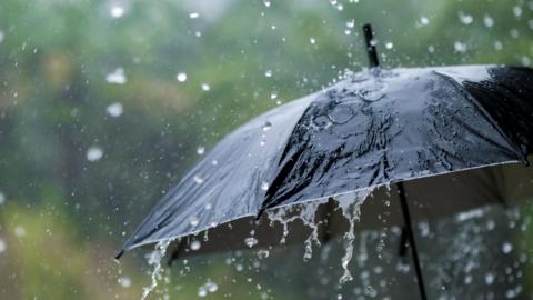 A stock image of rain falling on a black umbrella. 