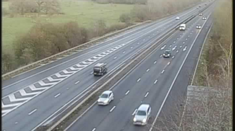 A traffic camera image of the A1(M) in Hertfordshire. Cars can be seen heading along the motorway with their headlights on during the early morning commute. 