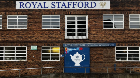 The brick building has many windows and a blue Royal Stafford sign with logo lower down at ground level.