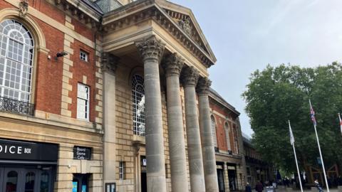 Peterborough Town Hall exterior image- with round pillars in front and flags raised in the background.
