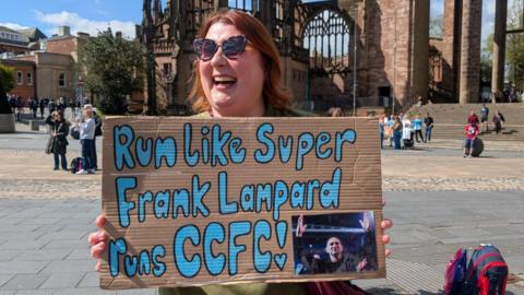 A smiling Kerry McGinty holds a sign reading "Run like super Frank Lampard runs CCFC"