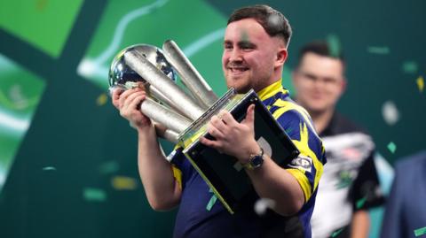Luke Littler holds the PDC World Championship trophy