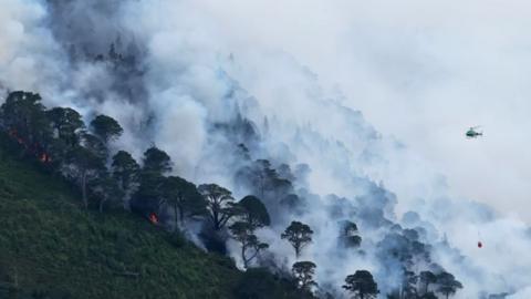 A vivid scene from the Cairngorms wildfire, with a helicopter flying over the fire