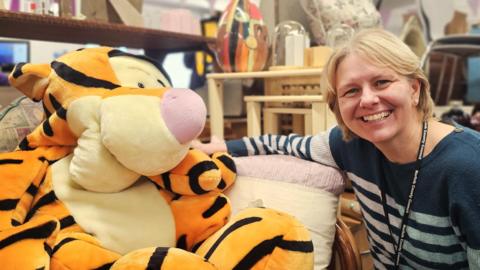 On the left side of the image we can see a large Tigger soft toy, with Martina on the right. She's wearing a blue and grey striped jumper.