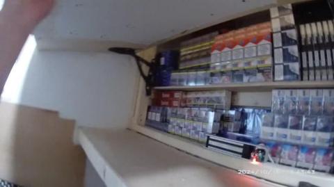 A cupboard full of illegal tobacco products and vapes. The still, taken from a police body camera, shows a hidden compartment being lifted open and packets of cigarettes stacked on a shelf.