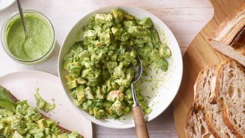 A white bowl filled with chicken and avocado in a green goddess sauce, with a loaf of sliced bread alongside.