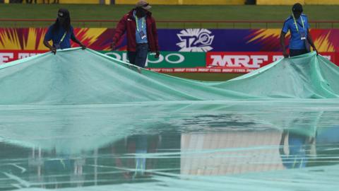 Ground staff inspect the covers after torrential rain