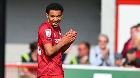 Kamari Doyle celebrates after scoring for Crawley Town, sticking out his tongue and rubbing his hands while dressed in Crawley's all-red home strip