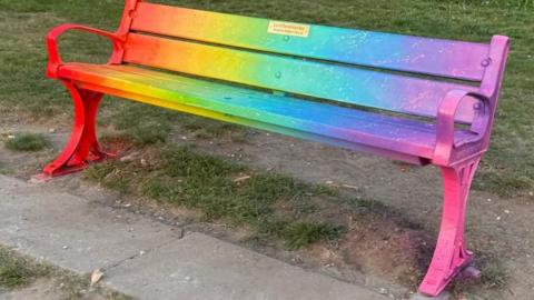 A park bench painted in different colours including yellow, pink and orange.