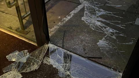 A glass door which has been smashed with glass on the floor inside the building.