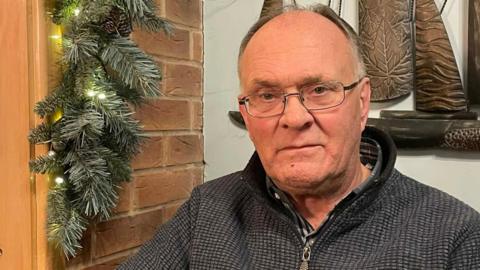 A man in late middle age stares at the camera