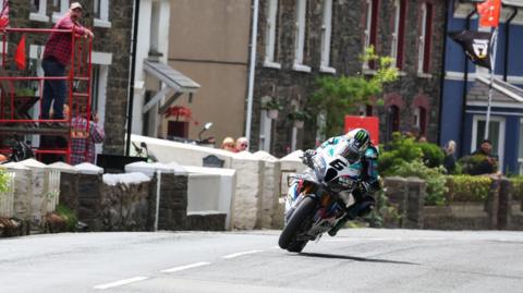 Michael Dunlop racing through Kirk Michael while spectators watch on from the front gardens of homes along the course.