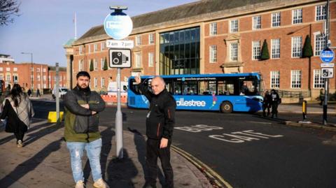 Taxi drivers Adnan Khan (left) and Lee Roach pointing to a bus lane sign in Derby city centre.