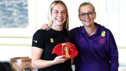 Poppy Pattinson holds her England cap alongside Sarina Wiegman