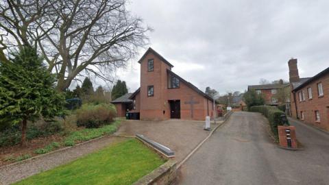 Malpas Community Church, a modern church building with a driveway to the side which leads to a car park. There is a low wall to the side, and a small grass area in front of the building.