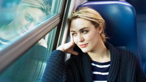 Blonde woman sitting on a train looking out the window
