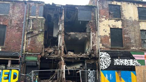 The front of the building has collapsed, showing the inside of the first and second floors of the derelict building