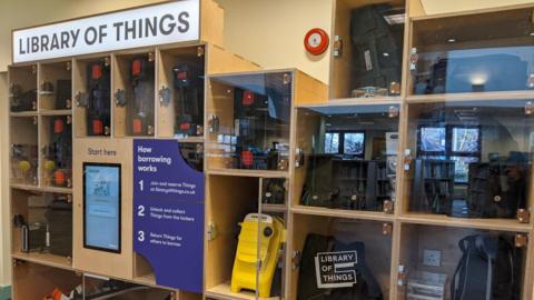 Electrical items locked in a cabinet and a sign of how people can register to borrow them