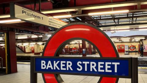 Image of a red and blue roundel sign for Baker Street, with the white tiled platform behind