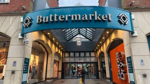 One of the entrances into the Buttermarket shopping Centre. A large sign details the name of the centre which proceeds to a large set of doors.