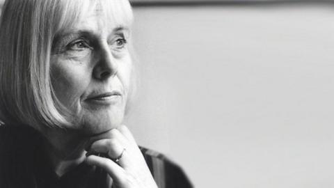 A black and white candid photo of a woman gazing at something away from the camera. There is a ring on her finger