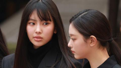 Close-up of Hyein and Haerin dressed in black, with long black hair