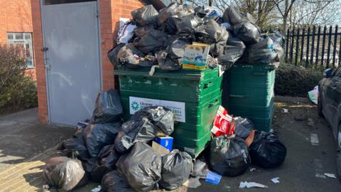 Black bin bags of rubbish on the floor and overflowing out of industrial bins