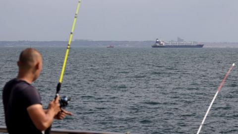 A fisherman watches the ship leave port