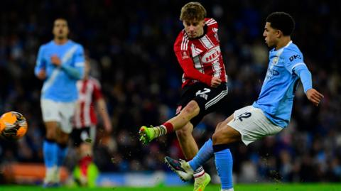 George Birch shooting with his left foot to score from outside the box against Manchester City as City defender Rico Lewis attempts to close him down.
