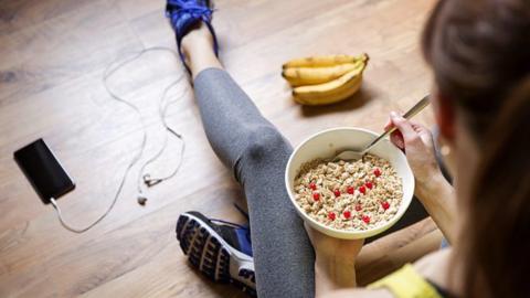 Someone in exercise clothes sitting on the floor eating from a bowl.
