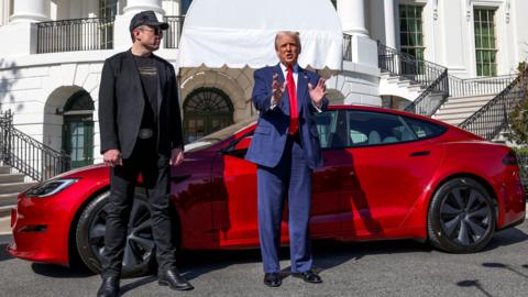 Elon Musk and Donald Trump stand in front of a red Tesla car which is parked in front of the White House in Washington D.C, United States. 