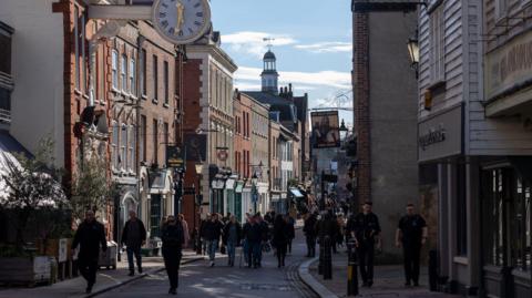 Rochester High Street. There are dozens of people walking down a road with shops either side of the road. 