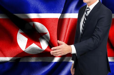 A man in a suit offering a handshake, with the North Korea flag in the background