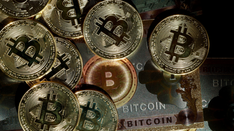 A visual representation of the Bitcoin cryptocurrency. The image shows mocked-up gold coins with a 'B' for Bitcoin on them, and silver, bronze and gold bank notes saying 'Bitcoin' on them.