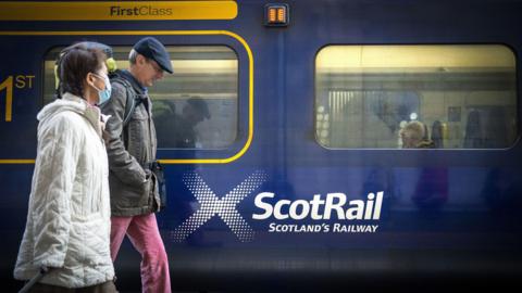 Commuters walk along the platform beside a Scotrail train.