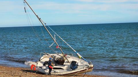 Empty vessel run ashore on Felpham beach with coastguard standing next to it
