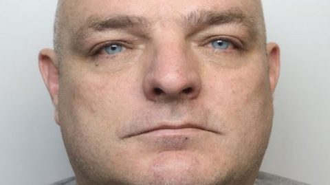 A mugshot of a man with a round face, far-apart eyes and a shaved head