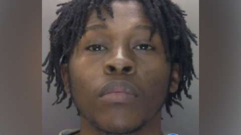 A police custody photo of Koketso Ximba, who is wearing a grey top and is in front of a grey wall