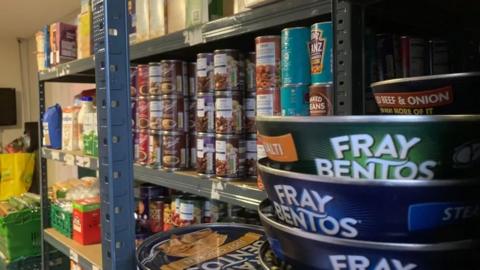 A large array of food cans on shelves and other produce in the background.