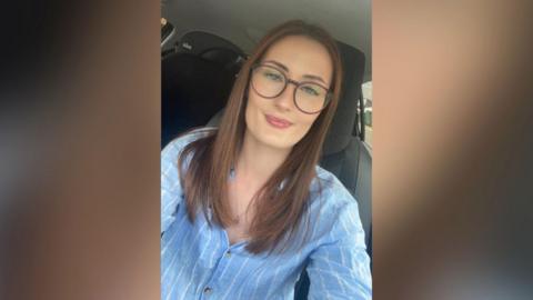 A woman wearing glasses and a blue shirt sitting in the front seat of a car