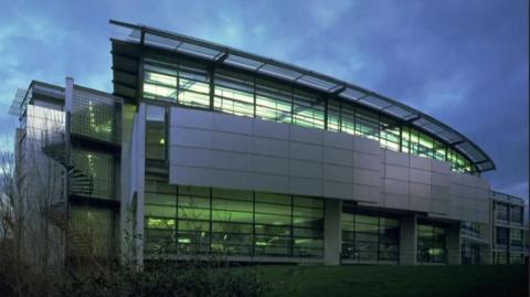 Four-storey metal and glass building lit up against a cloudy dusk