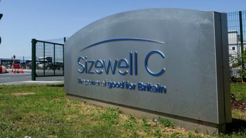 An entrance sign at the Sizewell C construction site in Leiston, Suffolk. It is a grey sign with blue writing that reads: Sizewell C the power of good for Britain.